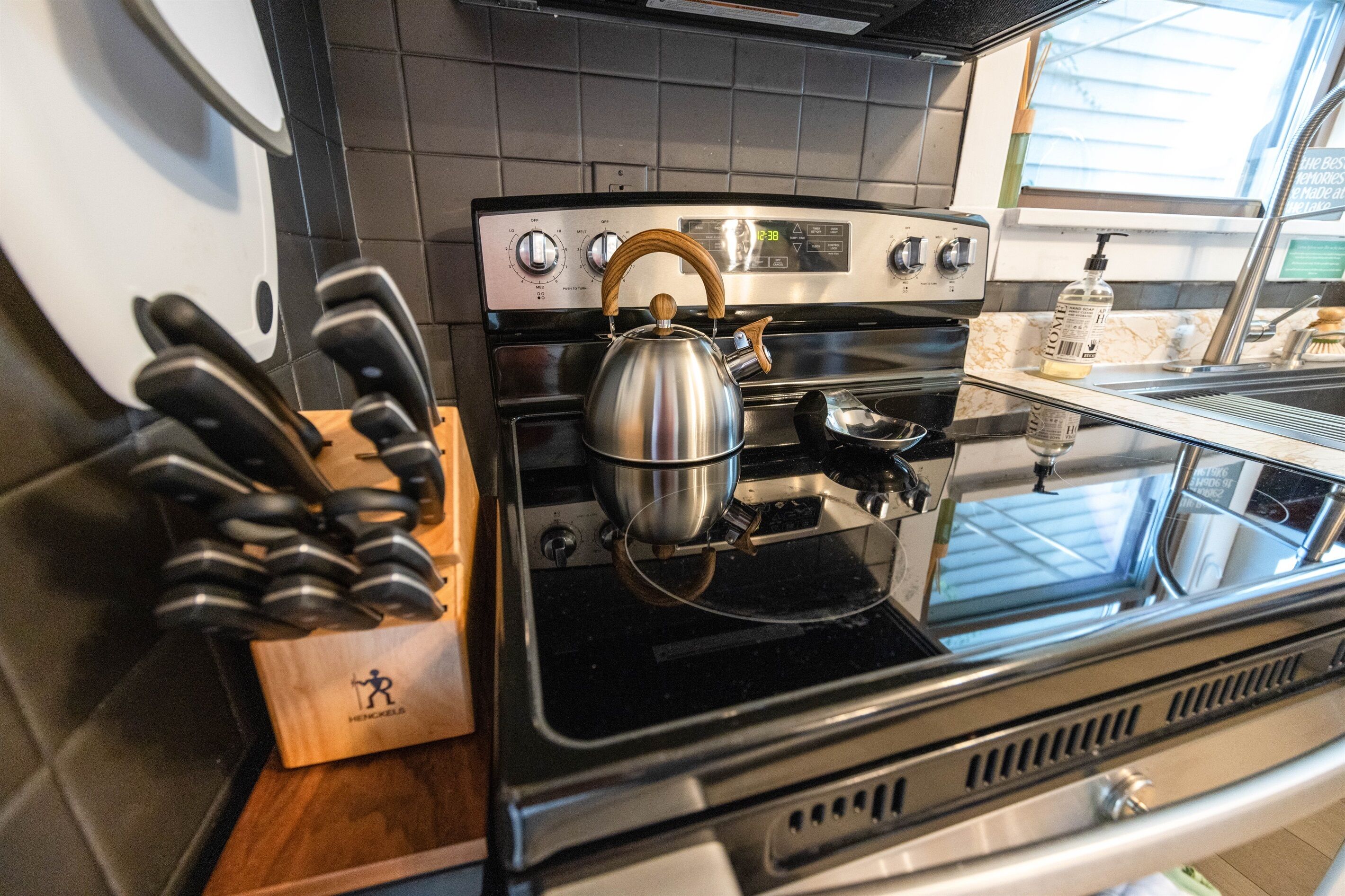 A kitchen with a stainless steel stove, a kettle, and a knife block.