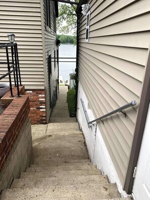 A narrow concrete staircase leading to a door, flanked by beige siding walls and a brick base. - Lake Front Retreat | Kayak | Paddleboard | Fishing (Decatur)