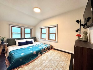 A bedroom with a bed, two windows, a nightstand, a lamp, and a wall-mounted shelf with decorative items. - Lake Front Retreat | Kayak | Paddleboard | Fishing (Decatur)