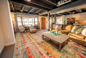 A cozy living room with a large window, a patterned rug, and a sofa with cushions.