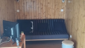 Una habitación con paredes de madera, un sofá, una mesita con un ordenador y un cubo.