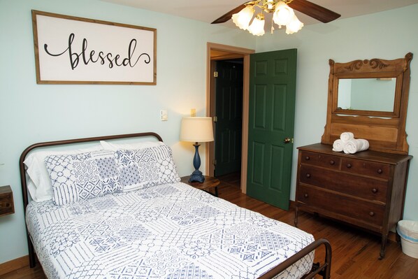Une chambre à coucher avec un lit, une commode, un miroir, une porte verte et un panneau décoratif sur le mur.