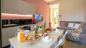 Una cocina moderna con horno empotrado, un comedor con una mesa dispuesta para el desayuno y una sala de estar con sofá y televisor.