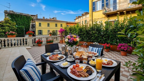 Una terraza con suelo a cuadros, mobiliario exterior, una mesa preparada para el desayuno y vistas a edificios con balcones.