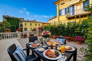 A terrace with a checkered floor, outdoor seating, a table set with breakfast, and a view of buildings with balconies. - Desenzanoloft Palazzo Visconti - Garda Chiaretto (Desenzano del Garda)
