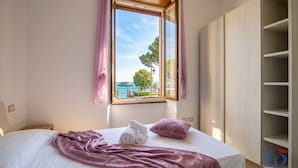 Un dormitorio con cama, ventana con cortinas y vistas al mar, además de un armario.