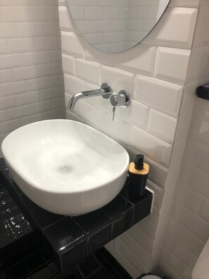 Casa de banho com lavatório branco, bancada preta e espelho em cima.