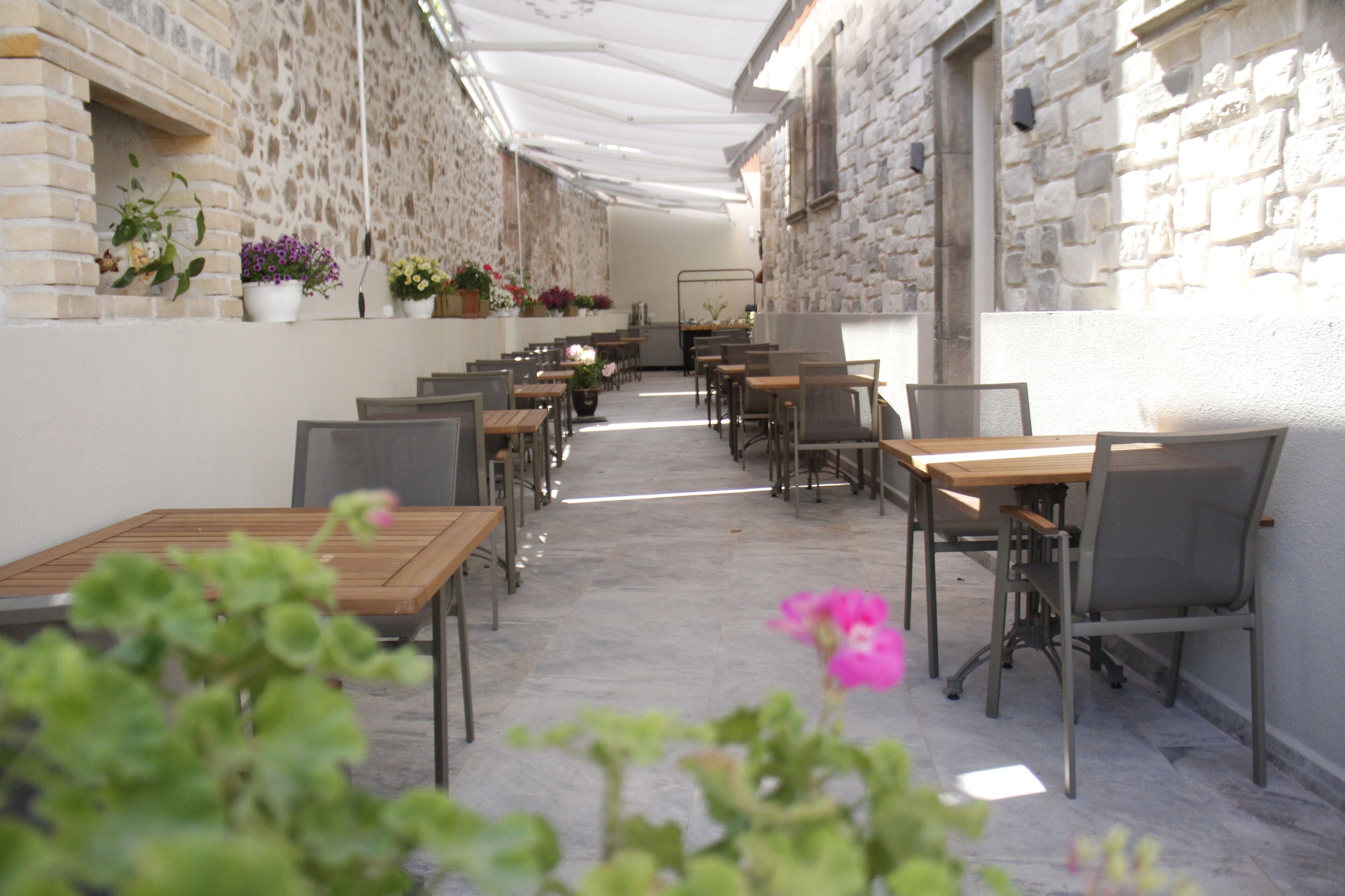 An outdoor café with tables and chairs arranged along a stone wall, under a white canopy.