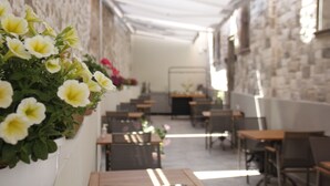 An indoor dining area with tables and chairs, a stone wall, and a row of yellow flowers on the left. - PetraAda Bozcaada (Bozcaada)