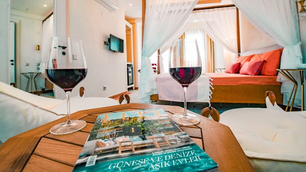 A room with a bed, a table with a magazine, and two glasses of red wine. - PetraAda Bozcaada (Bozcaada)