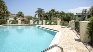 Ein Pool mit Liegestühlen und Palmen, umgeben von Gebäuden.