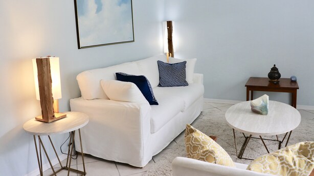 Ein modernes Wohnzimmer mit einem weißen Sofa, einem runden Couchtisch und einem Beistelltisch mit einer Lampe.