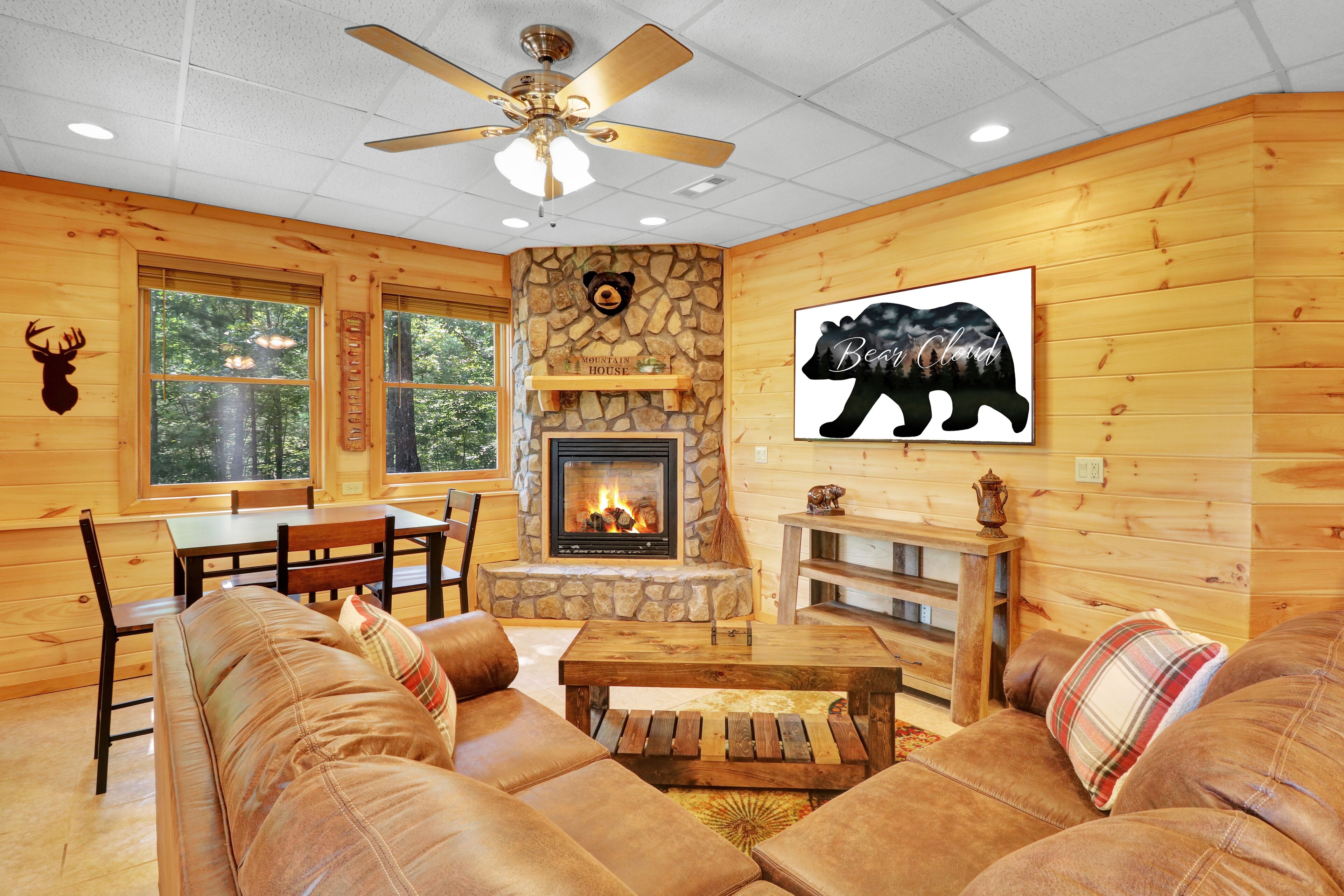 A cozy cabin interior with a stone fireplace, wooden walls, and a bear-themed artwork.