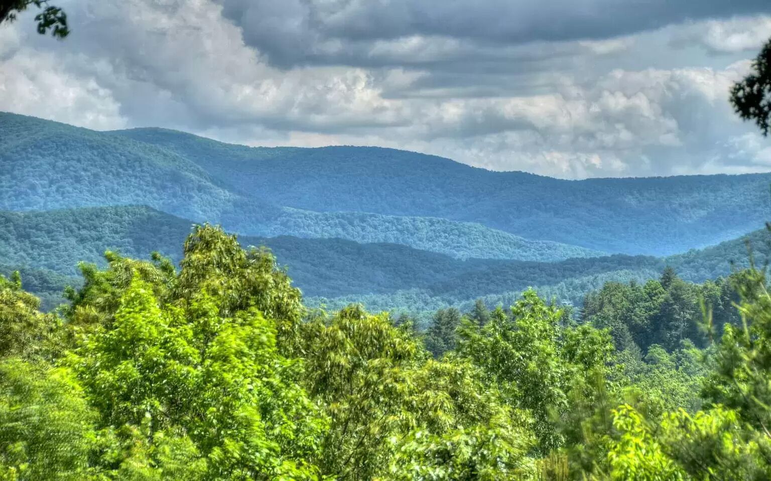 A mountainous landscape with dense green foliage and a cloudy sky.