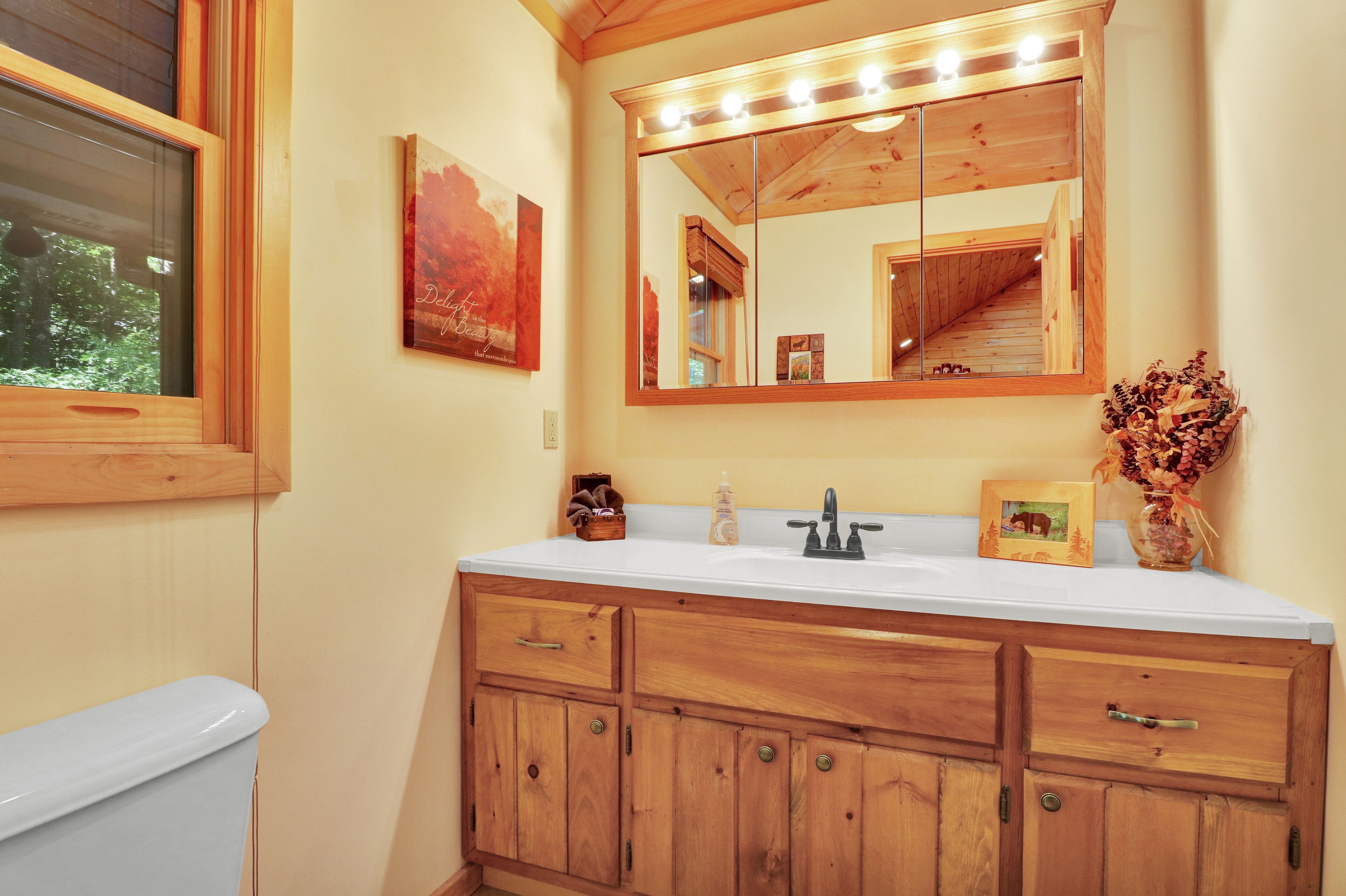 A bathroom with wooden cabinets, a white sink, and a large mirror with lights.