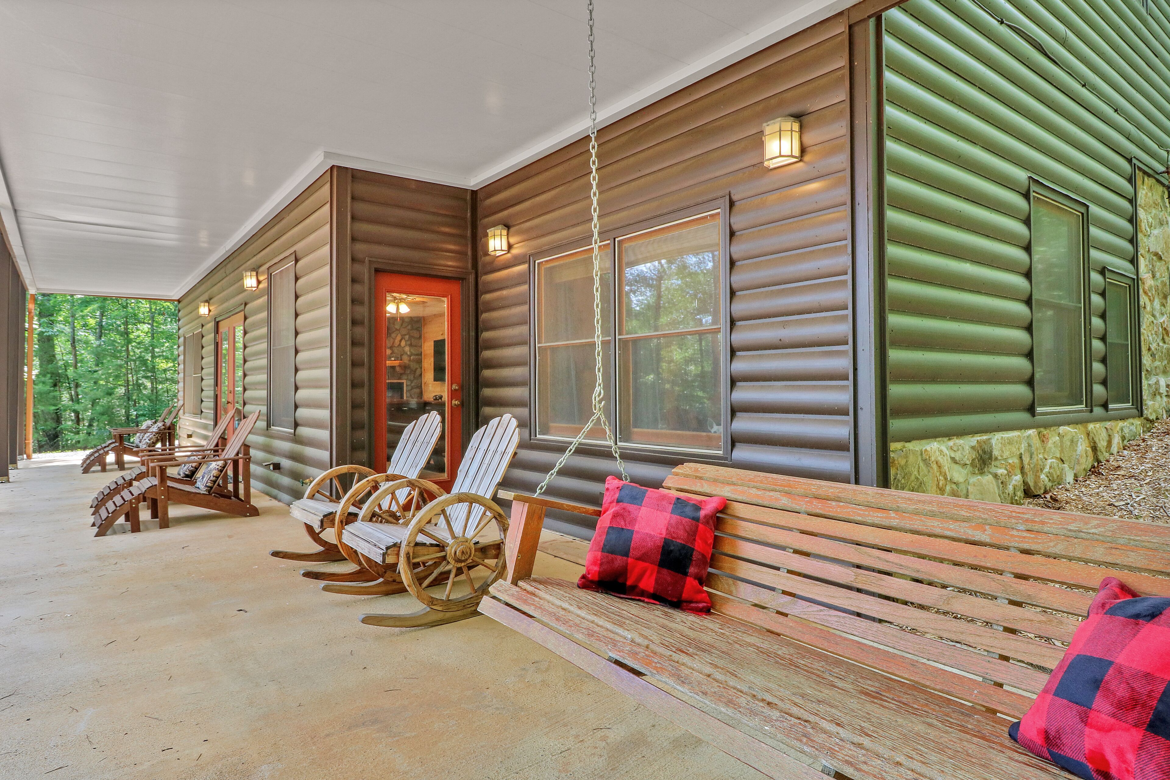 Een overdekte veranda met Adirondack-stoelen, een schommelstoel en een bank met geruite kussens.