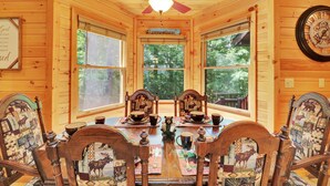 Une salle à manger aménagée dans une cabane en bois, avec une grande fenêtre, un ventilateur de plafond et une horloge au mur.