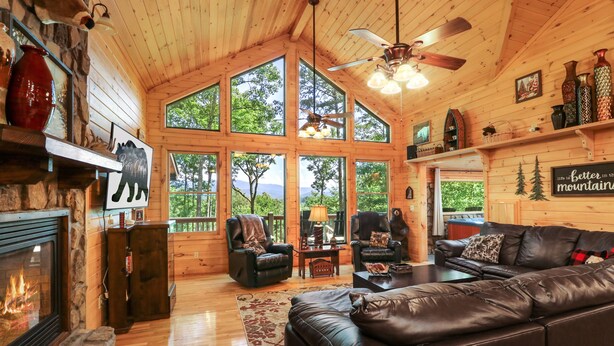 Un intérieur de chalet chaleureux avec une cheminée, des canapés en cuir et de grandes fenêtres donnant sur une vue imprenable sur les montagnes.