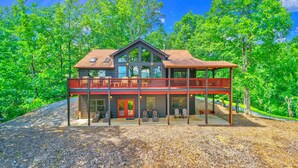 Une cabane en rondins à deux étages, dotée d’un balcon et entourée d’arbres.