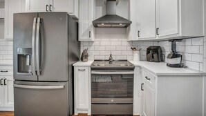Una cocina moderna con armarios blancos, un refrigerador de acero inoxidable, un horno y una cafetera.