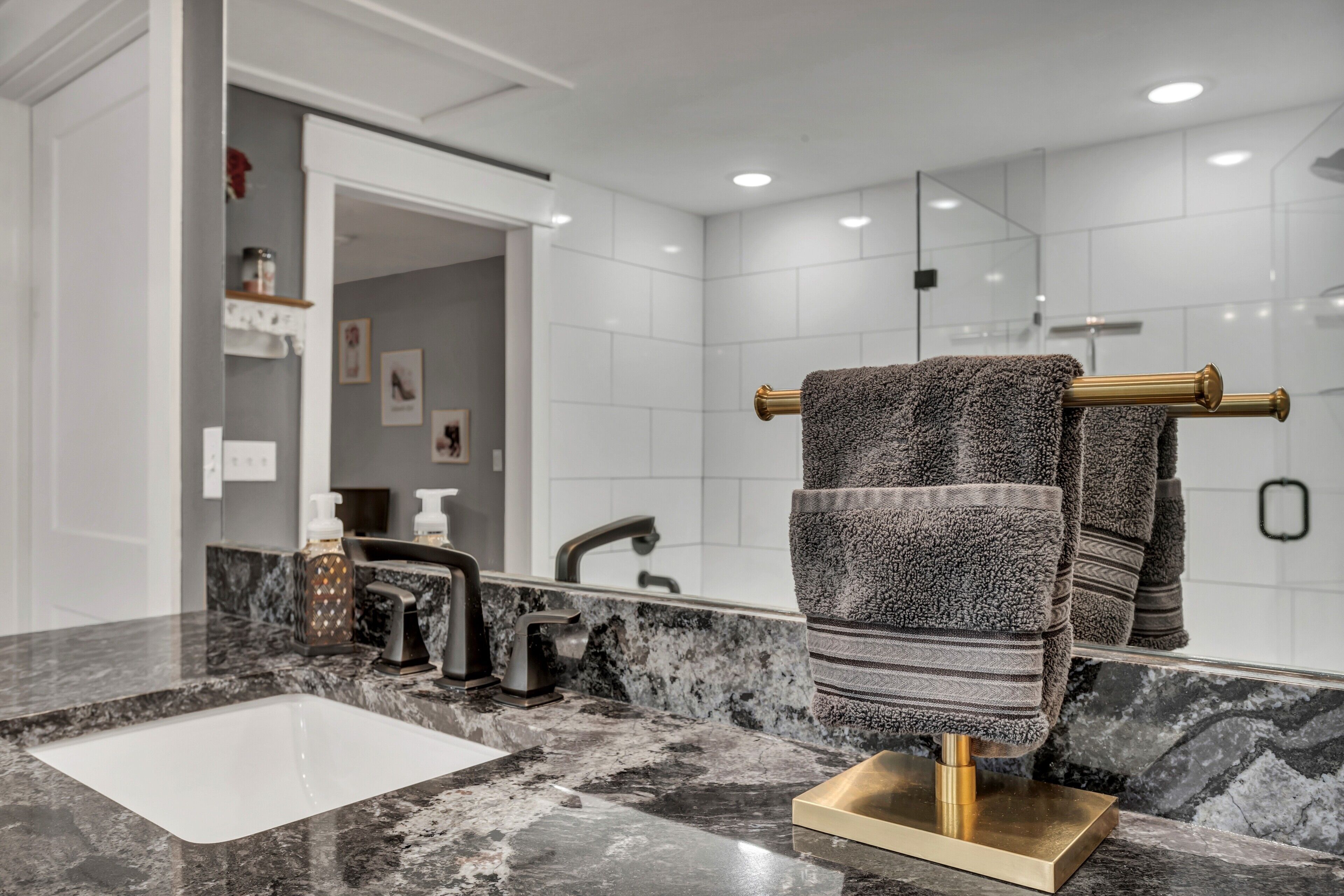 Un baño moderno con un lavabo de mármol, un perchero dorado y un espejo grande.