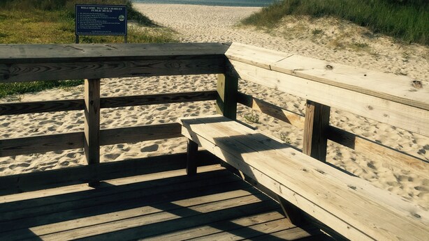 Una pasarela de madera que conduce a una playa arenosa, con un cartel que indica que es una playa pública.