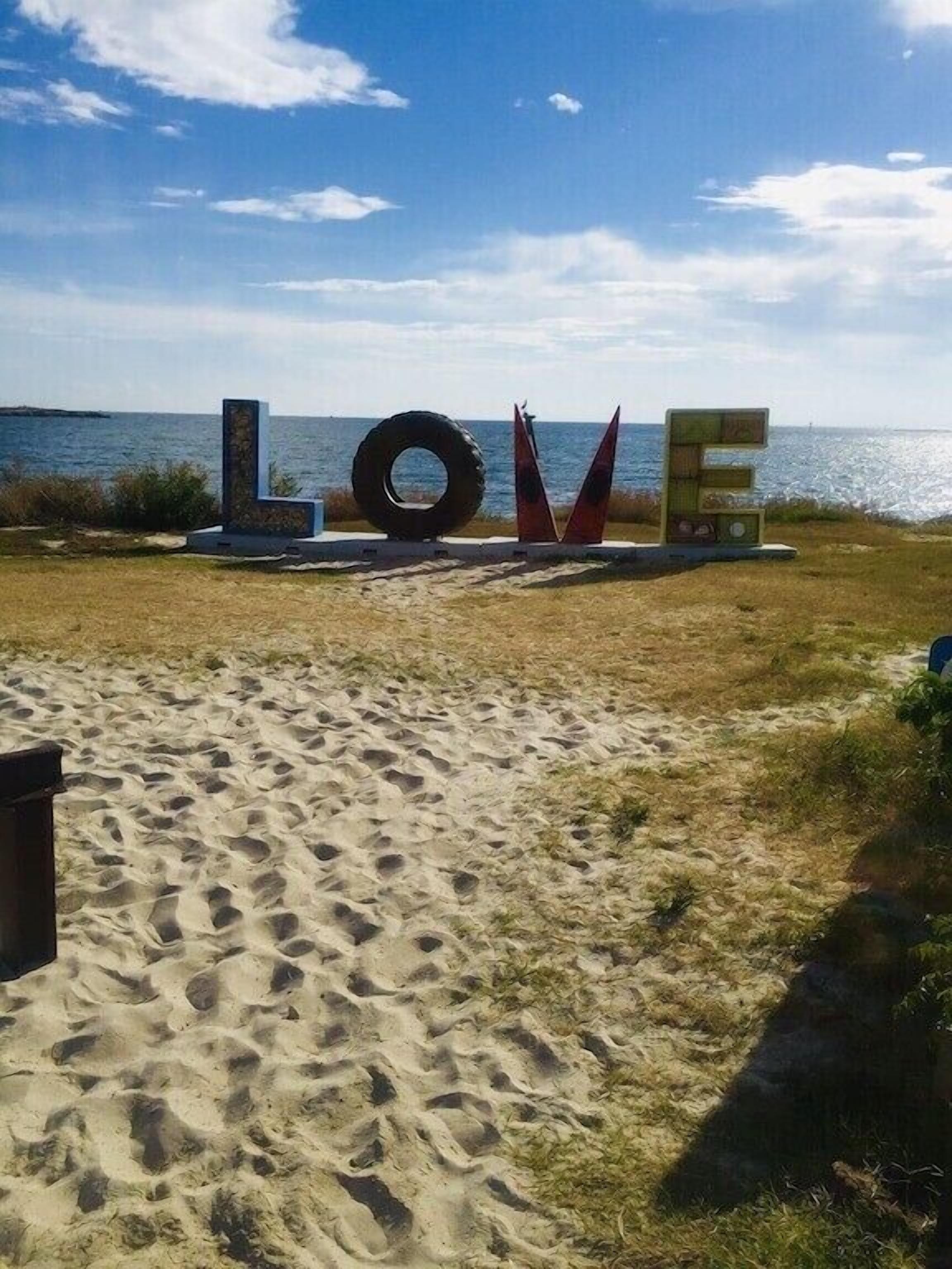 Une plage de sable où sont disposées de grandes lettres formant le mot « AMOUR » et une sculpture faite de pneus.