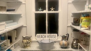 Una cocina con armarios blancos, un ventanal decorado con estrellas de mar y un letrero que dice "BEACH HOUSE".
