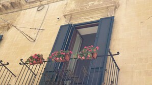 A building with a balcony featuring wrought iron railings and flower boxes with pink flowers. - DIMORA SANTA CROCE Newly renovated apartment in the historic center of Lecce (Lecce)