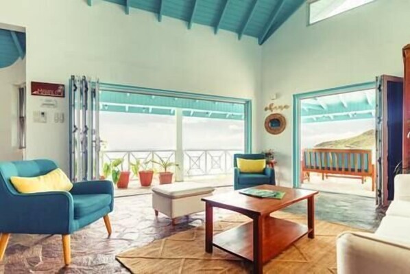 Habitación con vistas al mar, que incluye dos sillones azules, una mesa de centro de madera y una mesita auxiliar blanca.