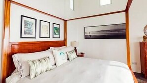Une chambre à coucher avec une tête de lit en bois, un grand lit recouvert de draps blancs et trois tableaux encadrés accrochés au mur.