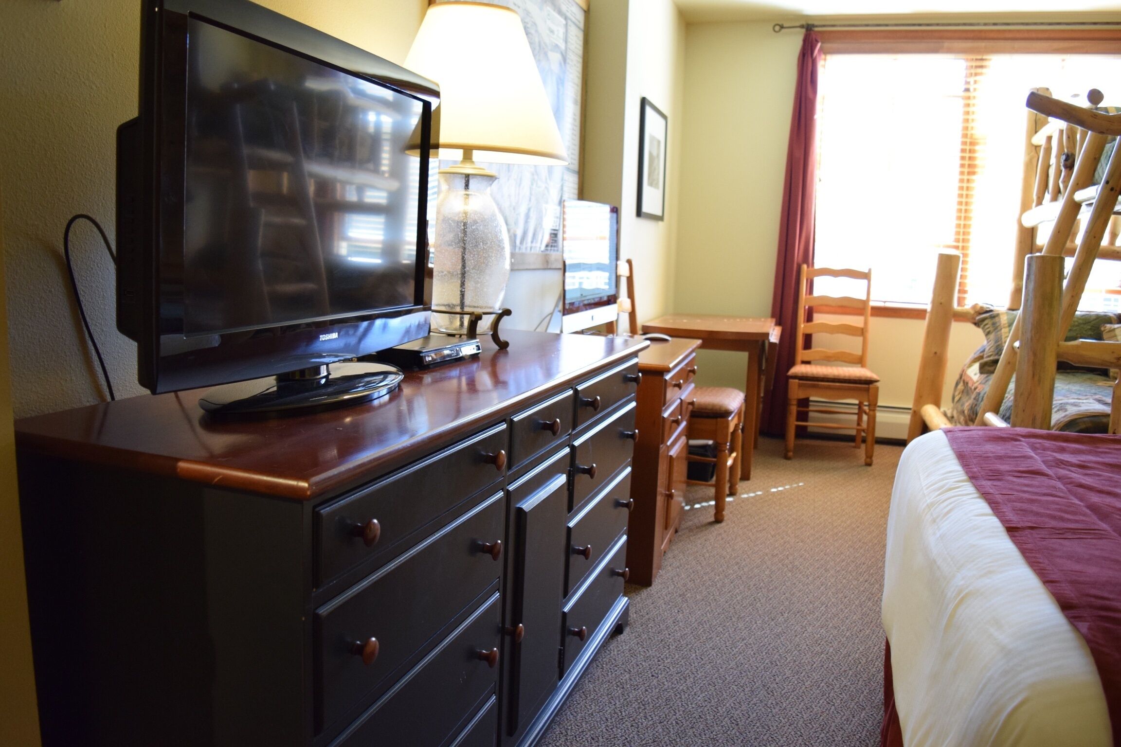 A hotel room with a bed, a desk with a lamp, a television, and a chair.
