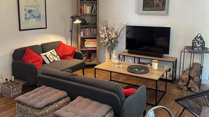 A modern living room with a sofa, ottomans, a coffee table, a bookshelf, a flat-screen TV, and a fireplace. - Villa des Genêts (Montagrier)