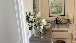A room with a wooden floor, a grey dresser, a mirror, a framed picture, and a vase with white flowers. - Villa des Genêts (Montagrier)