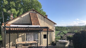 A house with a tiled roof, a covered patio with a table and chairs, and a view of the countryside. - Villa des Genêts (Montagrier)