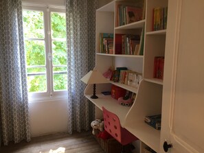 Ein Zimmer mit Bücherregal, einem fensterbepflanzten Fenster und einer Lampe.
