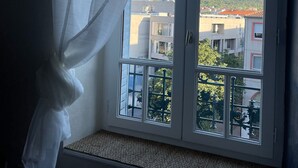 Habitación con ventana que da a una zona residencial, cortina blanca y vistas a edificios y zonas verdes.