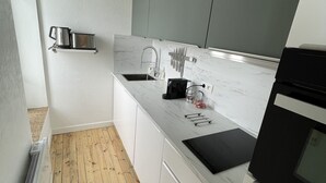 Una cocina moderna con armarios blancos, encimera de mármol, horno empotrado y suelo de madera.