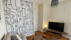 Una sala de estar moderna con un sofá gris, una mesa de centro de madera, una gran obra de arte abstracta en la pared, un televisor de pantalla plana y una lámpara colgante.
