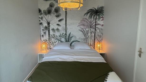Un dormitorio con una cama, dos lámparas de noche, un mural en la pared y una lámpara colgante.
