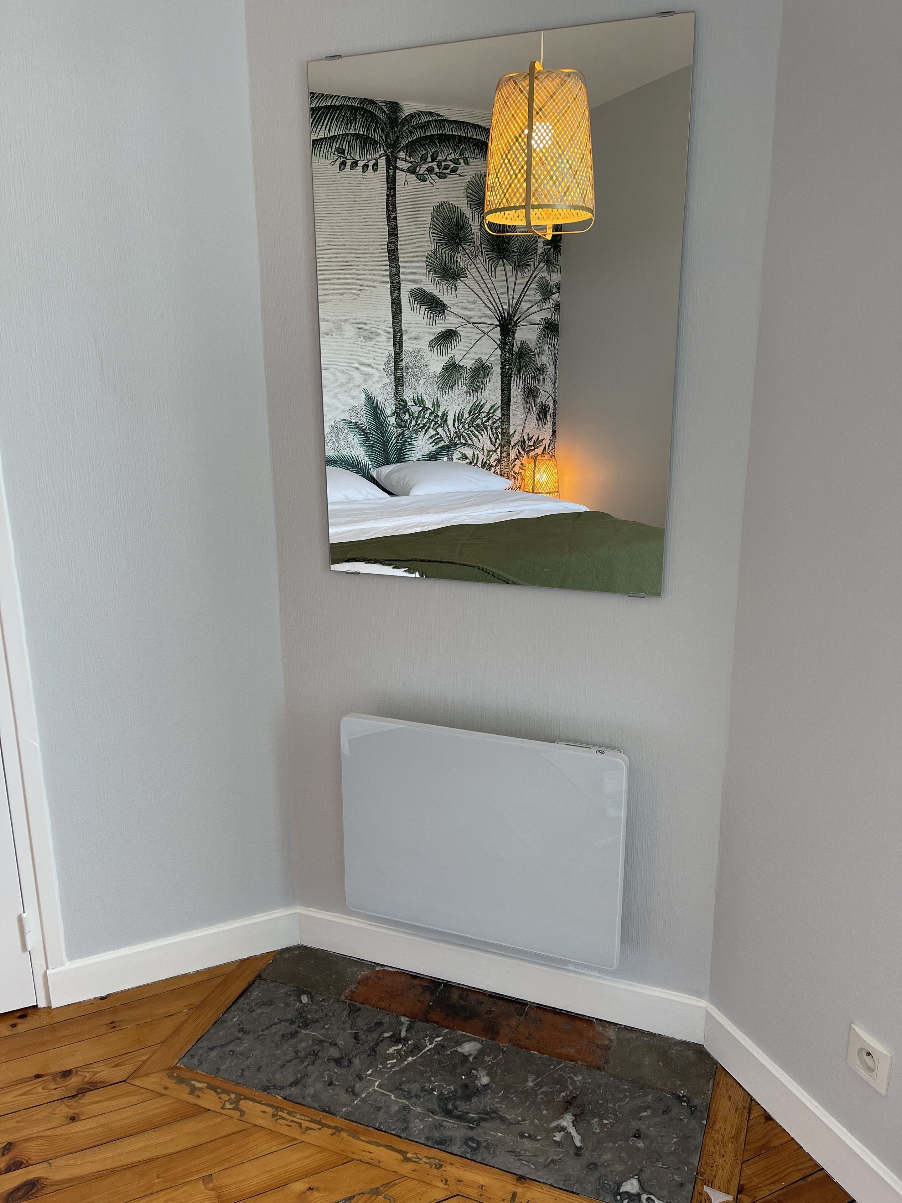 A room with a large mirror, a bed, a bench, and a floor with a mix of wooden and stone tiles.