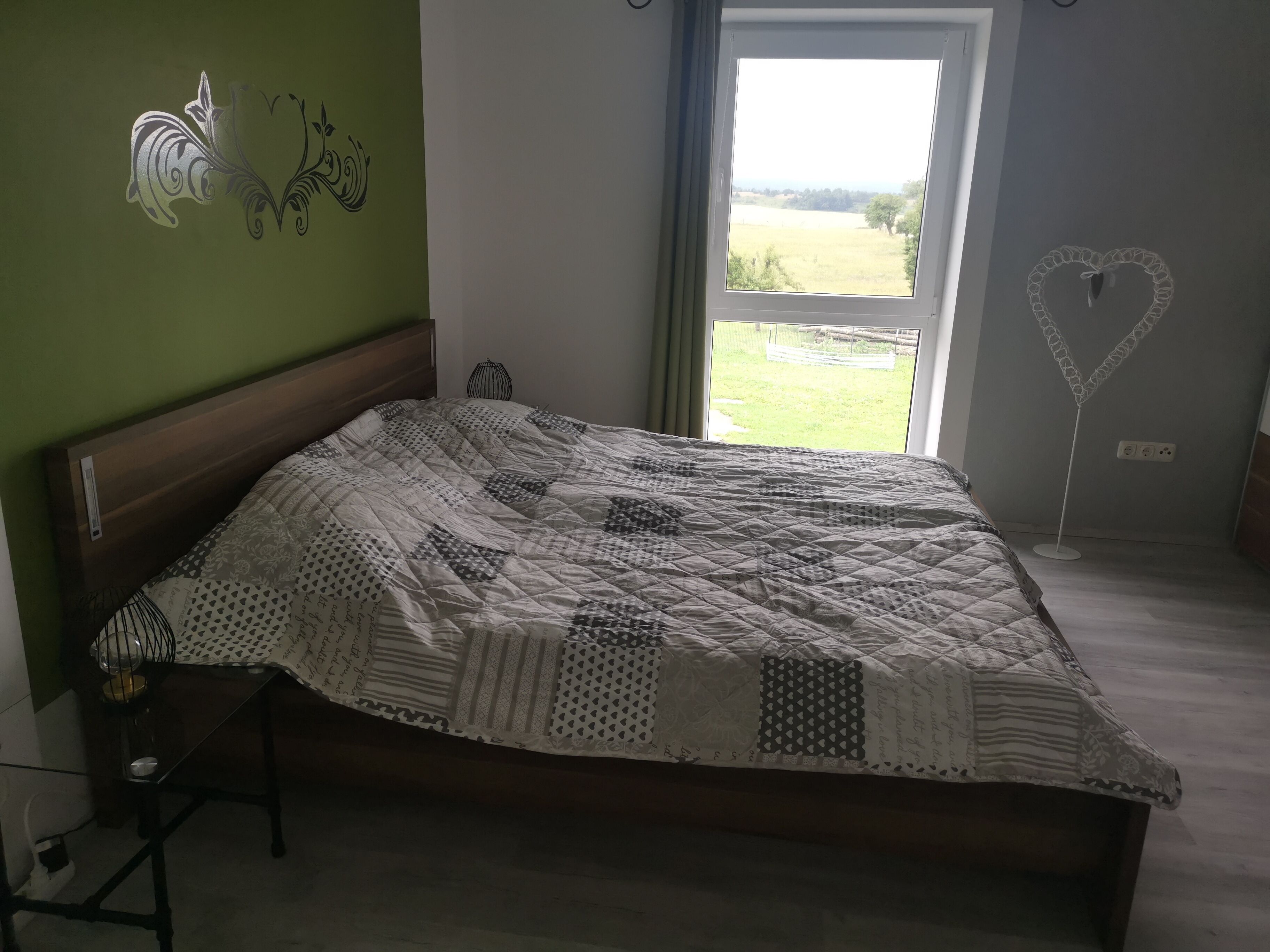A bedroom with a bed, a bedside table, a lamp, and a view of the outdoors.