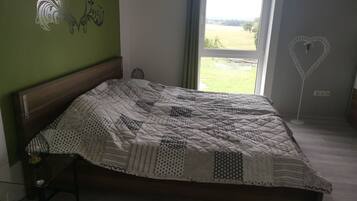 A bedroom with a bed, a bedside table, a lamp, and a view of the outdoors.