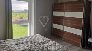 A bedroom with a large bed, a wardrobe, and a window with a view of a green landscape. - Panoramablick Nahe Oberhof (Geratal)
