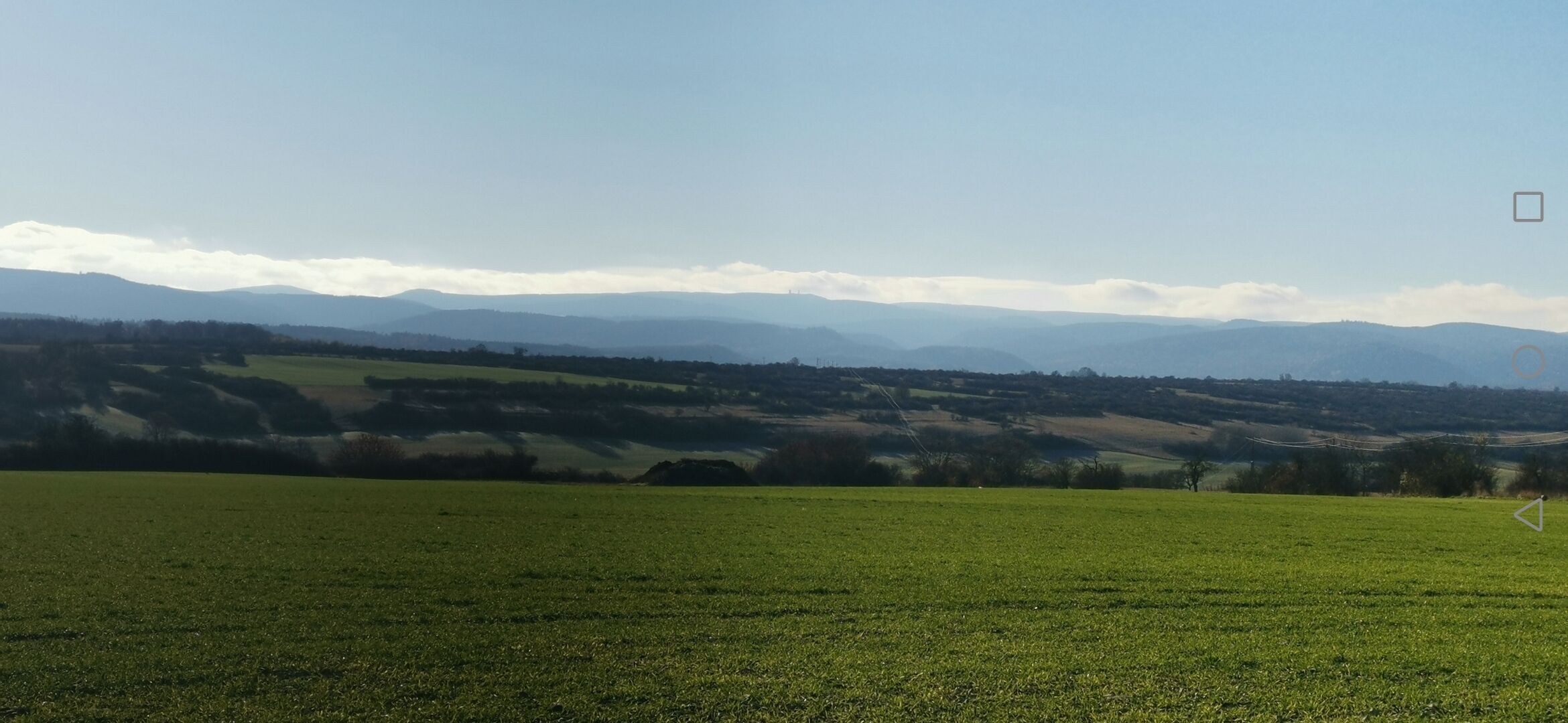 Un'ampia distesa verde con montagne lontane e cielo sereno.