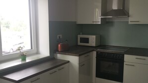 A compact kitchen with white cabinets, a microwave, a stove, and a window providing natural light. - Panoramablick Nahe Oberhof (Geratal)