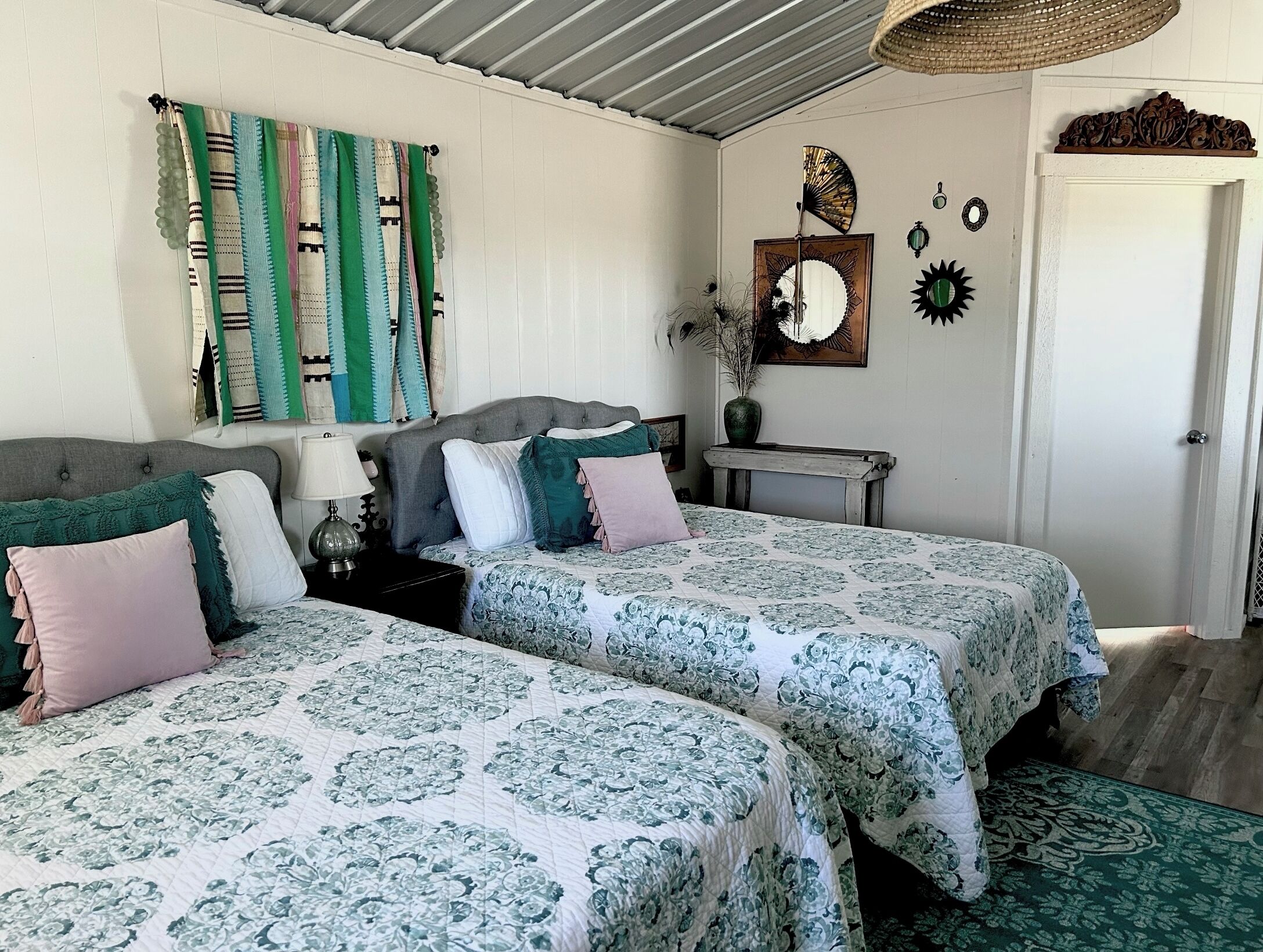 A bedroom with two beds, a bedside table, a lamp, a mirror, and wall decorations.