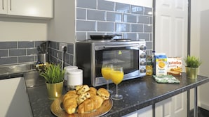 A kitchen with a toaster oven, a plate of croissants, a glass of orange juice, and a box of Nutella. - Tudors Inn Handsworth (Birmingham)