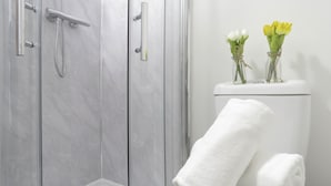 A bathroom with a glass shower enclosure, a toilet with a white towel, and two vases with flowers. - Tudors Inn Handsworth (Birmingham)