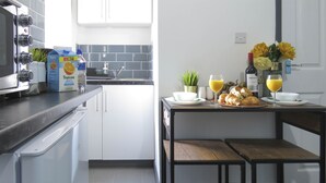 A modern kitchen with a built-in oven, a sink, and a dining area with a table set for breakfast. - Tudors Inn Handsworth (Birmingham)